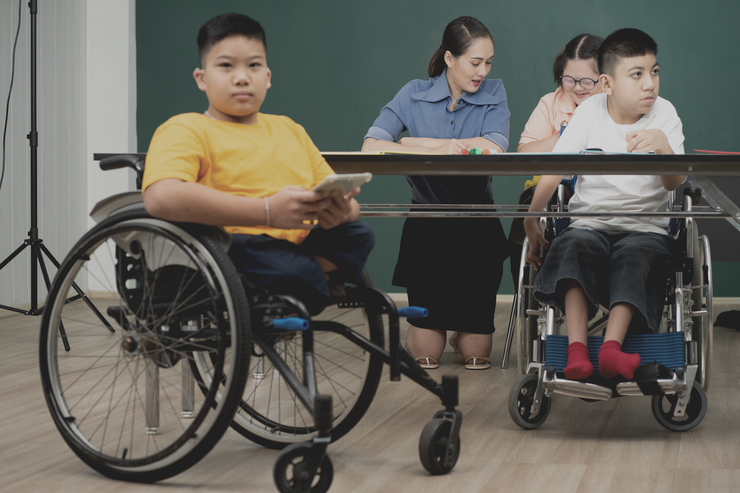 Disability kid on wheelchair in special classroom with AUtism children and teacher
